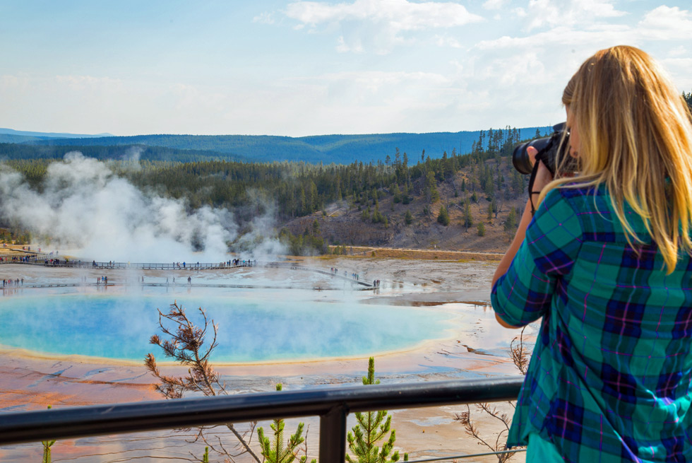 A summer bus tour passenger stops to take a photo of Grand Prismatic Springs